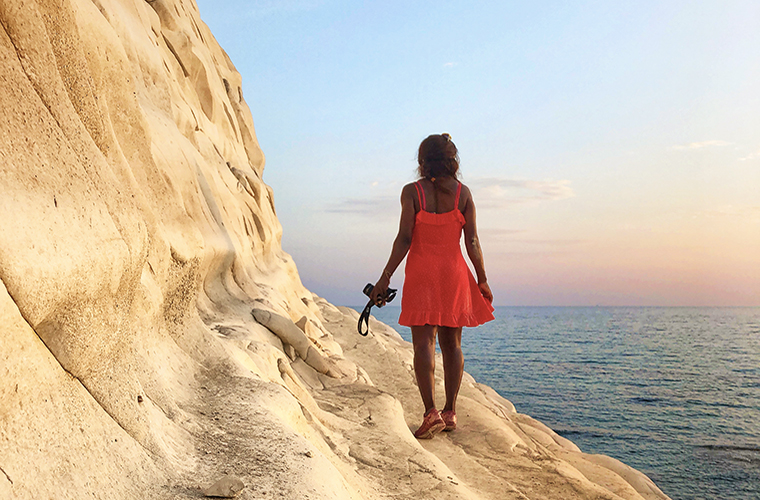Meltingsisters - why i choose to explore - a black girl dressed in a red dress standing on a white cliff and looking at the sea at sunset