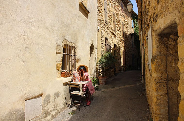 Meltingsisters - Lourmarin: the warmth of the old Provence - a girl sitting at a table in a narrow lane